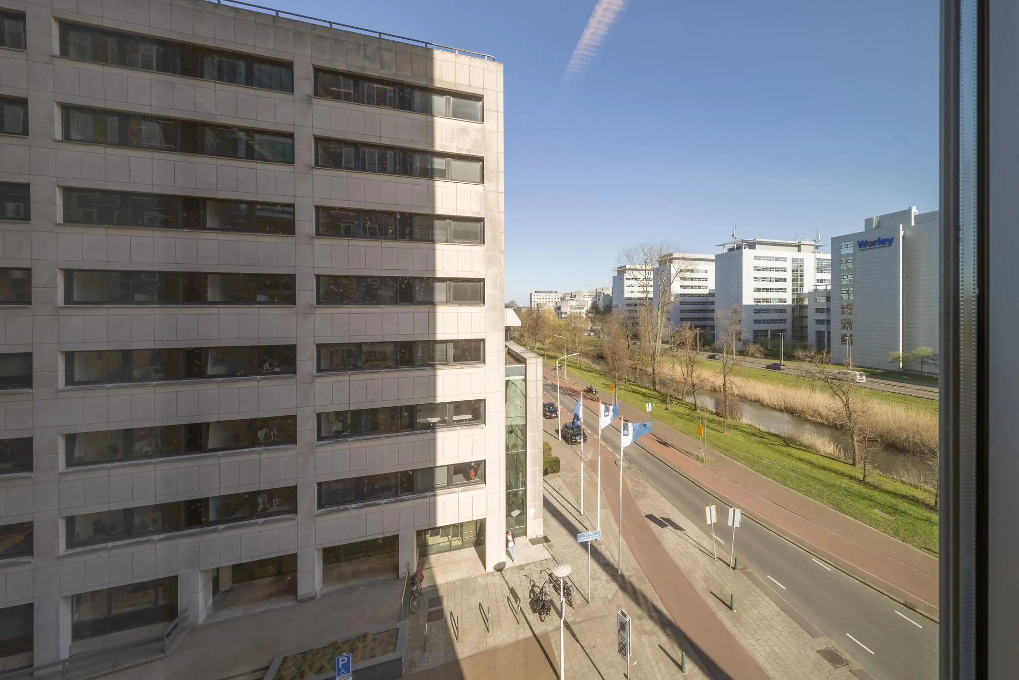 Uitzicht op de Prinses Beatrixlaan in Den Haag met kantoorgebouwen, fietspad en voorbijrijdend verkeer op een zonnige dag.